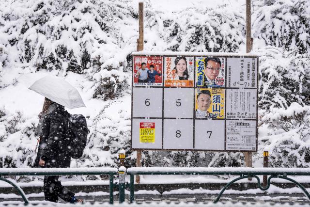 TOPSHOT - A woman walks past a board displaying posters of candidates for the House of Representatives election during a snowfall in Tokyo on February 8, 2026. Japan voted in snap elections February 8 with Prime Minister Sanae Takaichi hoping to turn a honeymoon start into a resounding ballot box victory that could rile China and rattle financial markets. (Photo by Yuichi YAMAZAKI / AFP)