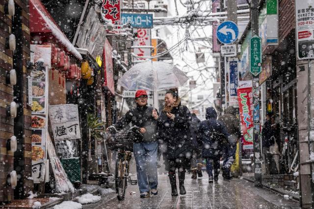 TOPSHOT - People walk through Nakano area during a snowfall in Tokyo on February 8, 2026. (Photo by Yuichi YAMAZAKI / AFP)