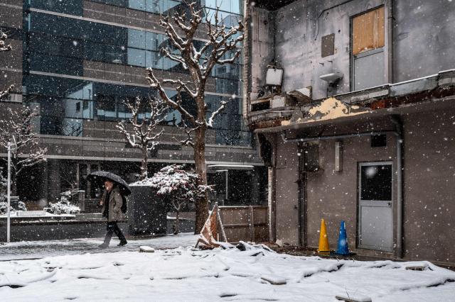 A pedestrian walks past an abandoned building during a snowfall in Tokyo's Chuo district on February 8, 2026. (Photo by Philip FONG / AFP)