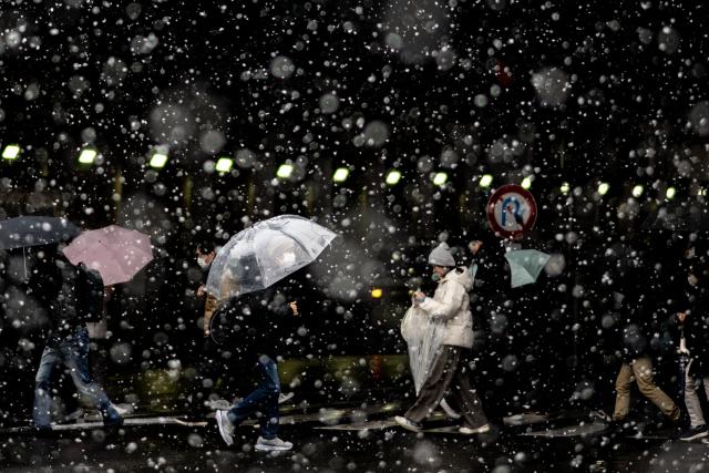 Pedestrians walk across a street underneath a railway bridge at Kinshicho station during a snowfall in Tokyo on February 8, 2026. (Photo by Philip FONG / AFP)