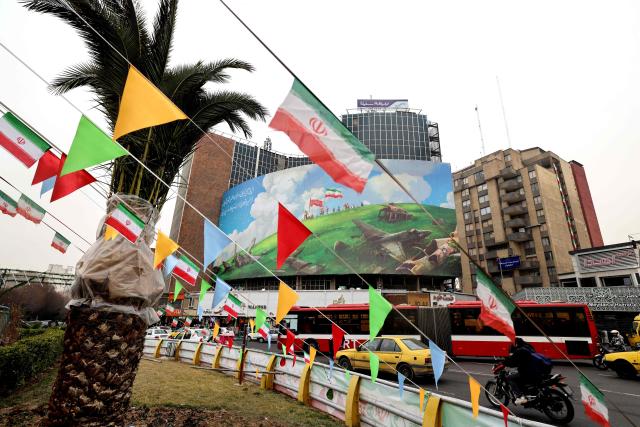 A passenger bus drives past a huge anti-US billboard displayed on a building in Tehran's Valiasr Square on February 8, 2026. (Photo by ATTA KENARE / AFP)