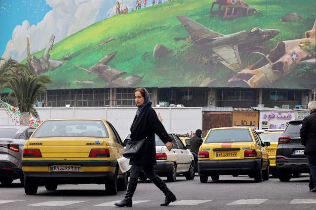 An Iranian woman walks past a huge anti-US billboard displayed on a building in Tehran's Valiasr Square on February 8, 2026. (Photo by ATTA KENARE / AFP)