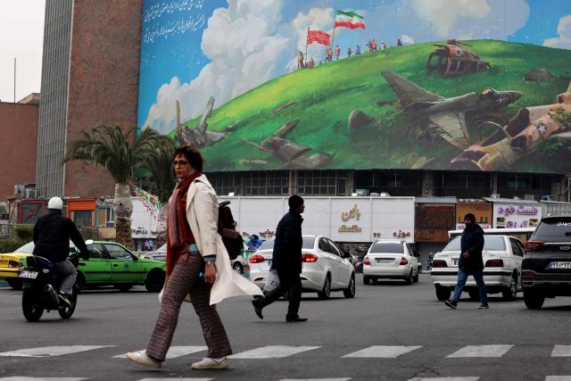 An Iranian woman walks past a huge anti-US billboard displayed on a building in Tehran's Valiasr Square on February 8, 2026. (Photo by ATTA KENARE / AFP)