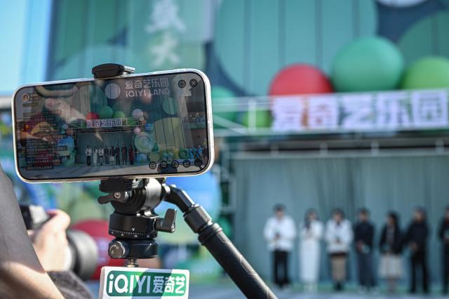 A phone screen shows a livestream of the opening ceremony of iQIYI LAND, a new entertainment theme park developed by China's online entertainment platform iQIYI, on its opening day in Yangzhou, in eastern China's Jiangsu province on February 8, 2026. (Photo by Jade GAO / AFP)