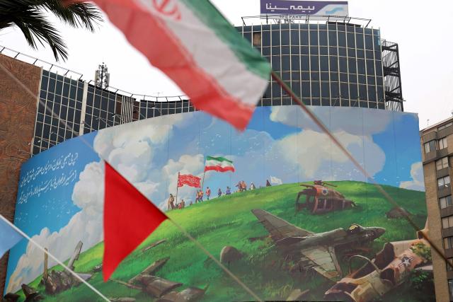 The Iranian flag flutters in front of a huge anti-US billboard displayed on a building in Tehran's Valiasr Square on February 8, 2026. (Photo by ATTA KENARE / AFP)