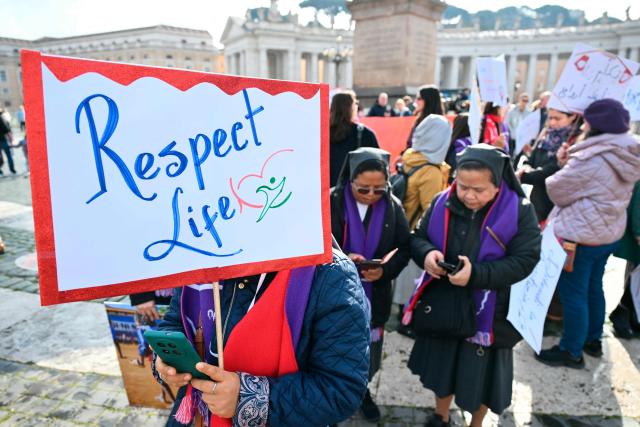 People hold placards to mark the International Day of prayer and awarness against Human Trafficking before at St. Peter's square before the Angelus prayer in The Vatican on February 8, 2026. (Photo by Alberto PIZZOLI / AFP)