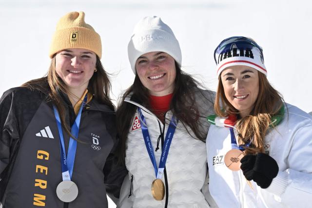 Gold medallist US' Breezy Johnson (C), silver medallist Germany's Emma Aicher (L) and bronze medallist Italy's Sofia Goggia (R) pose on the podium of the women's downhill event during the Milano Cortina 2026 Winter Olympic Games at the Tofane Alpine Skiing Centre in Cortina d’Ampezzo on February 8, 2026. (Photo by Tiziana FABI / AFP)