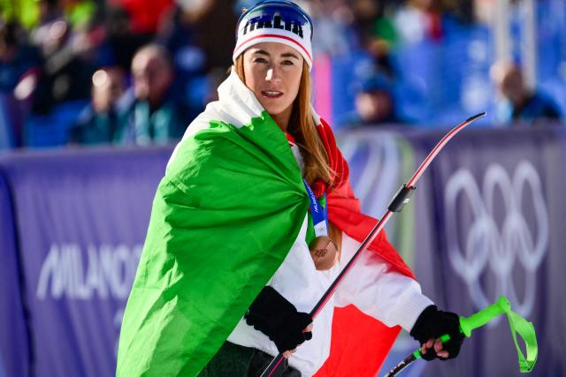 Italy's bronze medalist Sofia Goggia wears an Italian flag after the podium of the women's downhill event during the Milano Cortina 2026 Winter Olympic Games at the Tofane Alpine Skiing Centre in Cortina d’Ampezzo on February 8, 2026. (Photo by Stefano RELLANDINI / AFP)