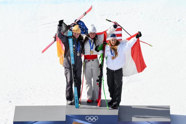 (From L) Silver medallist Germany's Emma Aicher, Gold medallist US' Breezy Johnson and bronze medallist Italy's Sofia Goggiaon pose with their national flags on the podium of the women's downhill event during the Milano Cortina 2026 Winter Olympic Games at the Tofane Alpine Skiing Centre in Cortina d’Ampezzo on February 8, 2026.  (Photo by Marco BERTORELLO / AFP)