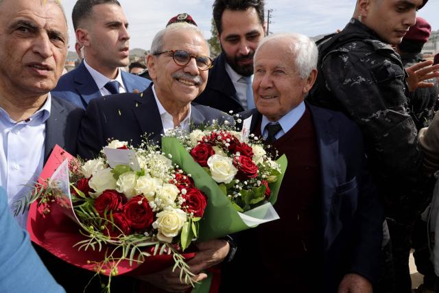 Lebanon's Prime Minister Nawaf Salam (L) holds bouquets of flower as he stands next to the mayor of the heavily-damaged southern village of Kfar Shouba, near the border with Israel, during his visit on February 8, 2026. Swathes of south Lebanon's border areas remain in ruins and largely deserted more than a year after a US-brokered November 2024 ceasefire sought to end hostilities between Israel and the Iran-backed group. Salam vowed authorities would begin key projects including restoring roads, communications networks and water in the two towns (Photo by Rabih DAHER / AFP)