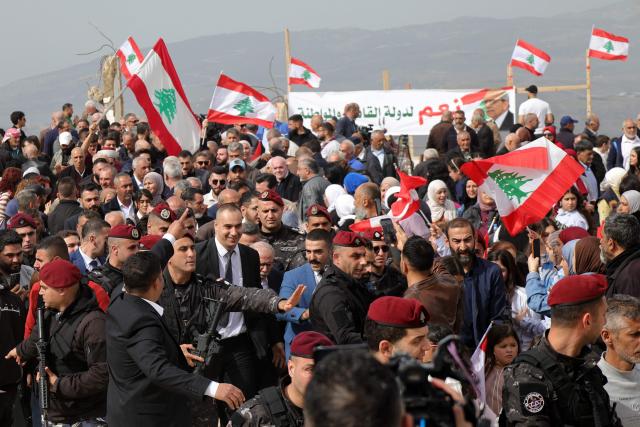 Residents wave the Lebanese flag as they wait for the arrival of Lebanon's prime minister during his visit ot the  heavily-damaged southern village of Kfar Shouba, near the border with Israel, on February 8, 2026. Swathes of south Lebanon's border areas remain in ruins and largely deserted more than a year after a US-brokered November 2024 ceasefire sought to end hostilities between Israel and the Iran-backed group. Salam vowed authorities would begin key projects including restoring roads, communications networks and water in the two towns (Photo by Rabih DAHER / AFP)