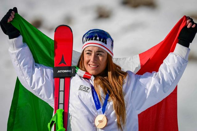 Italy's Sofia Goggia holds up an Italian flag as she wears her bronze medal on the podium of the women's downhill event during the Milano Cortina 2026 Winter Olympic Games at the Tofane Alpine Skiing Centre in Cortina d’Ampezzo on February 8, 2026. (Photo by Stefano RELLANDINI / AFP)