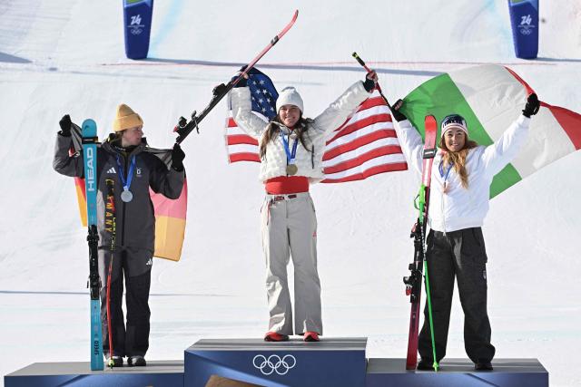 Gold medallist US' Breezy Johnson (C), silver medallist Germany's Emma Aicher (L) and bronze medallist Italy's Sofia Goggia (R) pose on the podium of the women's downhill event during the Milano Cortina 2026 Winter Olympic Games at the Tofane Alpine Skiing Centre in Cortina d’Ampezzo on February 8, 2026. (Photo by Tiziana FABI / AFP)