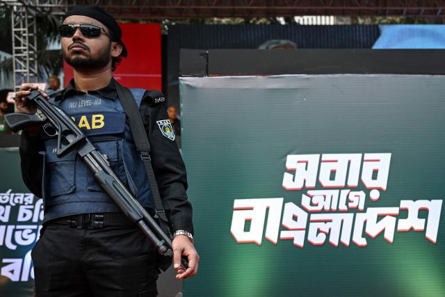 A Rapid Action Battalion (RAB) personnel stands guard next to a board with the slogan 'Bangladesh First' during an election rally of the Bangladesh Nationalist Party (BNP) ahead of the country's general election in Dhaka on February 8, 2026. Bangladesh's elections next week could reshape South Asia's balance of power, as Beijing seeks to consolidate influence and ties with India falter, analysts say. (Photo by Sajjad HUSSAIN / AFP)