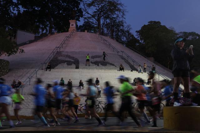 Runners pass by a mosaic depicting the eyes of late Venezuelan president Hugo Chavez on the stairs at Calvario Square as they take part in the 21 km and 42 km races of the 10th edition of the CAF Marathon in Caracas on February 8, 2026. (Photo by Pedro MATTEY / AFP)