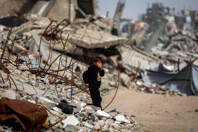 A boy blows a bubblegum while walking past destroyed buildings in the Jabalia camp for Palestinian refugees in the northern Gaza Strip on February 8, 2026. Since October 10, a fragile US-sponsored truce in Gaza has largely halted the fighting between Israeli forces and Hamas, but both sides have alleged frequent violations. (Photo by Omar AL-QATTAA / AFP)