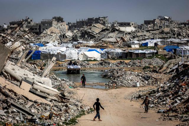 Boys walk past the rubble of destroyed buildings in the Jabalia camp for Palestinian refugees in the northern Gaza Strip on February 8, 2026. Since October 10, a fragile US-sponsored truce in Gaza has largely halted the fighting between Israeli forces and Hamas, but both sides have alleged frequent violations. (Photo by Omar AL-QATTAA / AFP)