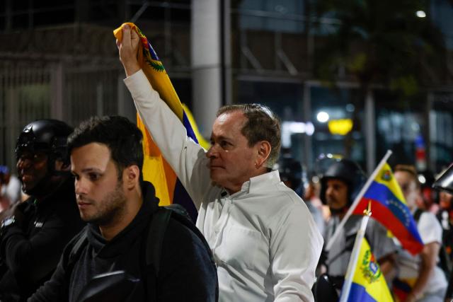 Venezuelan political leader Juan Pablo Guanipa (R) waves a national flag as he rides as a passenger on a motorbike after his release from Helicoide prison in Caracas on February 8, 2026. Two opposition figures close to Venezuela's Nobel peace laureate Maria Corina Machado were freed from jail on February 8, 2026, one month after authorities began releasing political prisoners following the ouster of leader Nicolas Maduro. (Photo by Pedro MATTEY / AFP)