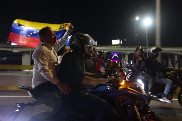 Venezuelan political leader Juan Pablo Guanipa (R) waves a national flag as he rides as a passenger on a motorbike after his release from Helicoide prison in Caracas on February 8, 2026. Two opposition figures close to Venezuela's Nobel peace laureate Maria Corina Machado were freed from jail on February 8, 2026, one month after authorities began releasing political prisoners following the ouster of leader Nicolas Maduro. (Photo by Pedro MATTEY / AFP)