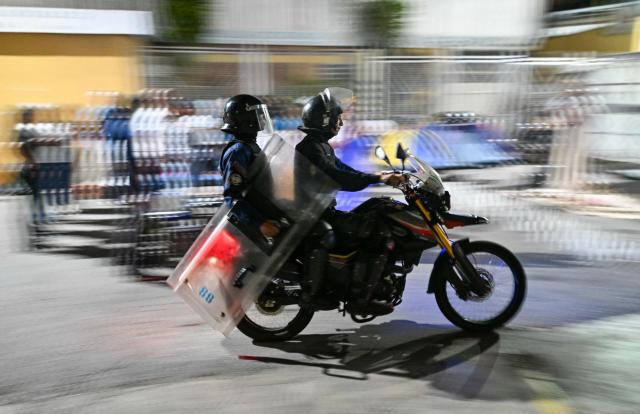 Venezuelan riot police officers ride a motorbike past a demonstration to demand the release of political prisoners outside Zona 7 prison in Caracas on February 8, 2026. Two opposition figures close to Venezuela's Nobel peace laureate Maria Corina Machado were freed from jail on February 8, 2026, one month after authorities began releasing political prisoners following the ouster of leader Nicolas Maduro. (Photo by Juan BARRETO / AFP)