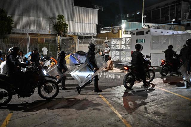 Venezuelan riot police officers pass by a demonstration to demand the release of political prisoners outside Zona 7 prison in Caracas on February 8, 2026. Two opposition figures close to Venezuela's Nobel peace laureate Maria Corina Machado were freed from jail on February 8, 2026, one month after authorities began releasing political prisoners following the ouster of leader Nicolas Maduro. (Photo by Juan BARRETO / AFP)