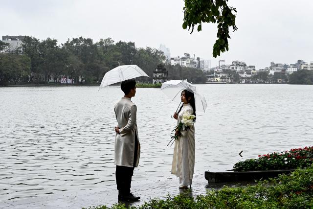 A couple holding umbrellas poses for photos at Hoan Kiem Lake in Hanoi on February 9, 2026. (Photo by Nhac NGUYEN / AFP)