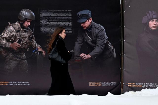 A woman walks past posters, featuring soldiers, displayed by the National Institute of National Remembrance as part of an open air exhibition in the center of Kyiv on February 8, 2026, amid the Russian invasion in Ukraine. (Photo by Sergei SUPINSKY / AFP)