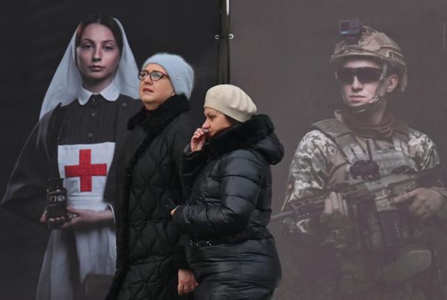 Women walk past a poster displayed by the National Institute of National Remembrance as part of an open air exhibition in the center of Kyiv on February 8, 2026, amid the Russian invasion in Ukraine. (Photo by Sergei SUPINSKY / AFP)