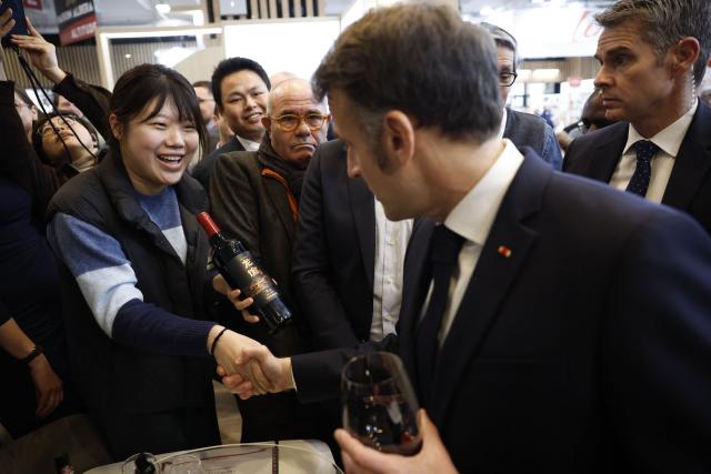 A Chinese winemaker presents a bottle of wine to France's President Emmanuel as he visits the Wine Paris 2026 fair at the Porte de Versailles exhibition centre in Paris on February 9, 2026. (Photo by Yoan VALAT / POOL / AFP)