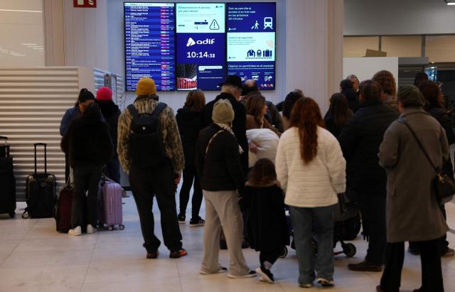 Commuters look at time table at Madrid's Chamartin train station, on February 9, 2026, amid a national strike by Spanish train drivers' union to demand railway safety measures following deadly accidents, in Adamuz and in Gelida. The sign reads 'If there were no more trains?'. Spanish train drivers began a three-day strike, demanding greater safety for their profession after two accidents claimed 47 lives last month, leaving thousands of passengers stranded. (Photo by Pierre-Philippe MARCOU / AFP)