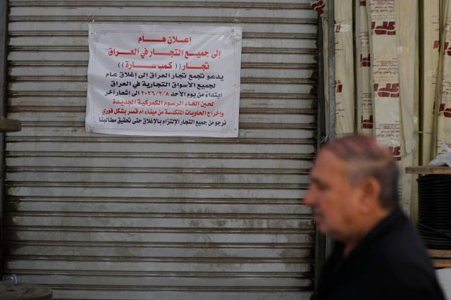 A photograph shows a poster calling on shop owners to strike, pasted on the shutters of a closed retail store selling electrical appliances, during a strike protesting an increase in customs tariffs on non-essential goods, in Baghdad on February 9, 2026. (Photo by AHMAD AL-RUBAYE / AFP)