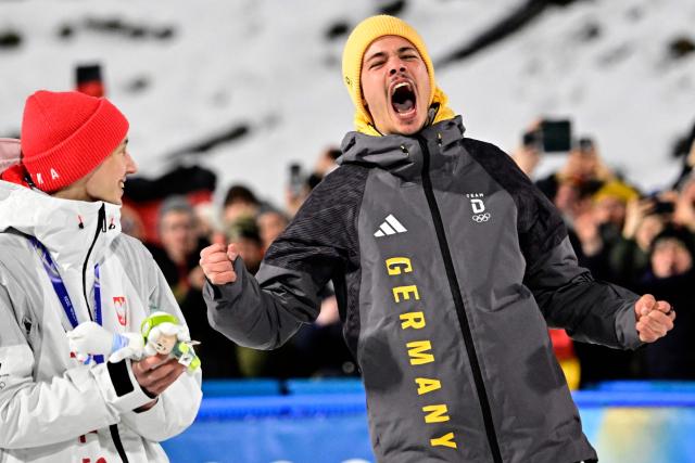 Gold medallist Germany's Philipp Raimund celebrates on the podium next to silver medallist Poland's Kacper Tomasiak (L) after winning the men's ski jumping normal hill individual final round of the Milano Cortina 2026 Winter Olympic Games at Predazzo Ski Jumping Stadium in Predazzo (Val di Fiemme), on February 9, 2026. (Photo by Tobias SCHWARZ / AFP)