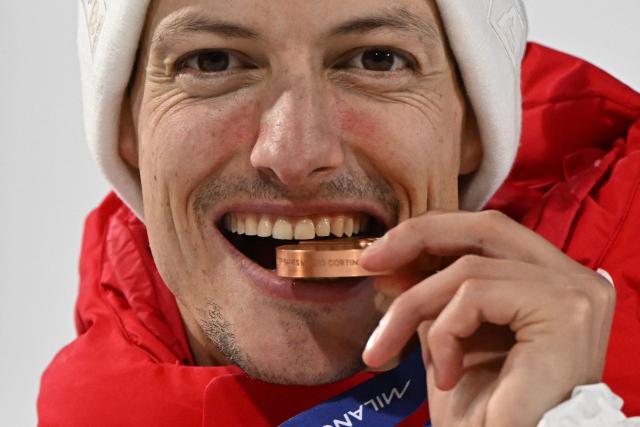 Bronze medallists who tied for third place Switzerland's Gregor Deschwanden bites his medal as he celebrates on the podium for the men's ski jumping normal hill individual final round of the Milano Cortina 2026 Winter Olympic Games at Predazzo Ski Jumping Stadium in Predazzo (Val di Fiemme), on February 9, 2026. (Photo by Javier SORIANO / AFP)