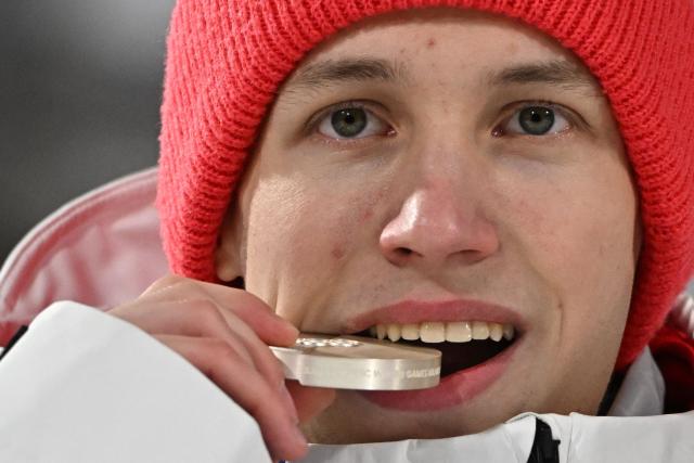 Silver medallist Poland's Kacper Tomasiak bites his medal as he celebrates on the podium after the men's ski jumping normal hill individual final round of the Milano Cortina 2026 Winter Olympic Games at Predazzo Ski Jumping Stadium in Predazzo (Val di Fiemme), on February 9, 2026. (Photo by Javier SORIANO / AFP)
