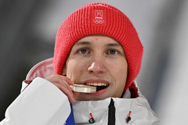 Silver medallist Poland's Kacper Tomasiak bites his medal as he celebrates on the podium after the men's ski jumping normal hill individual final round of the Milano Cortina 2026 Winter Olympic Games at Predazzo Ski Jumping Stadium in Predazzo (Val di Fiemme), on February 9, 2026. (Photo by Javier SORIANO / AFP)