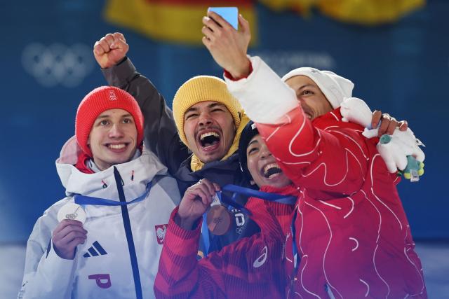 (From L) Silver medallist Poland's Kacper Tomasiak, gold medallist Germany's Philipp Raimund and Bronze medallists who tied for third place Japan's Ren Nikaido and Switzerland's Gregor Deschwanden take a selfie photo as they celebrate on the podium for the men's ski jumping normal hill individual final round of the Milano Cortina 2026 Winter Olympic Games at Predazzo Ski Jumping Stadium in Predazzo (Val di Fiemme), on February 9, 2026. (Photo by Anne-Christine POUJOULAT / AFP)