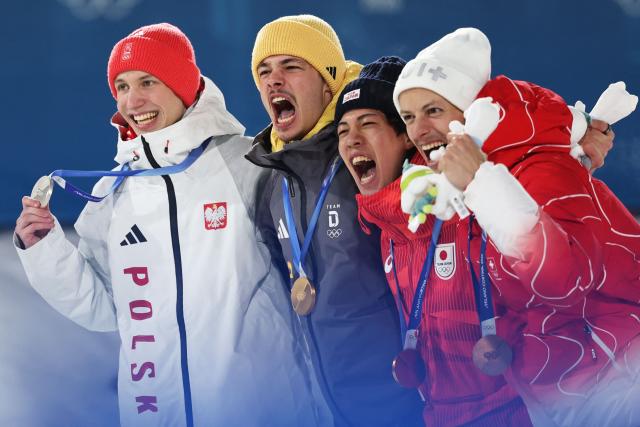 (From L) Silver medallist Poland's Kacper Tomasiak, gold medallist Germany's Philipp Raimund and Bronze medallists who tied for third place Japan's Ren Nikaido and Switzerland's Gregor Deschwanden celebrate on the podium for the men's ski jumping normal hill individual final round of the Milano Cortina 2026 Winter Olympic Games at Predazzo Ski Jumping Stadium in Predazzo (Val di Fiemme), on February 9, 2026. (Photo by Anne-Christine POUJOULAT / AFP)