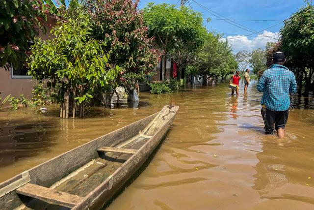 TOPSHOT - People walk on a flooded street in Lorica, Cordoba department, Colombia on February 9, 2026. At least 13 deaths were reported this week in different parts of Colombia due to the intense rains battering the country, which are unusual for this time of year, according to a report on February 8, 2026, based on official information. (Photo by AFP)