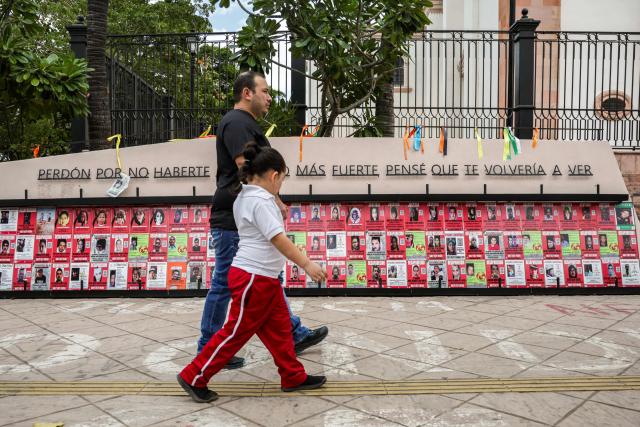 A man and a girl walk past a memorial for victims of enforced disappearance in downtown Culiacan, Sinaloa state, Mexico, on February 9, 2026. Three of the 10 employees of a Canadian mining company who were kidnapped two weeks ago in Mexico's violence-plagued Sinaloa state have been found dead, Mexico's Mining Chamber said on February 9. (Photo by Jesus Verdugo / AFP)