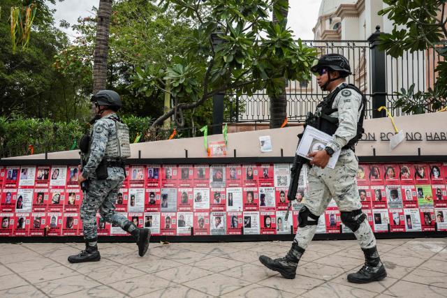 National Guard officers walk past a memorial for victims of enforced disappearance in downtown Culiacan, Sinaloa state, Mexico, on February 9, 2026. Three of the 10 employees of a Canadian mining company who were kidnapped two weeks ago in Mexico's violence-plagued Sinaloa state have been found dead, Mexico's Mining Chamber said on February 9. (Photo by Jesus Verdugo / AFP)