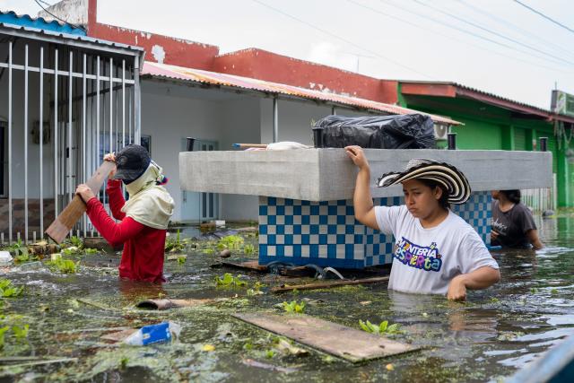 People carry belongings on a flooded street in Monteria, Colombia on February 9, 2026. At least 13 deaths were reported this week in different parts of Colombia due to the intense rains battering the country, which are unusual for this time of year, according to a report on February 8, 2026, based on official information. (Photo by AFP)