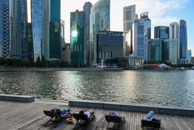 People relax on beach chairs along the boardwalk during sunset at Marina Bay in Singapore on February 9, 2026. (Photo by Roslan RAHMAN / AFP)