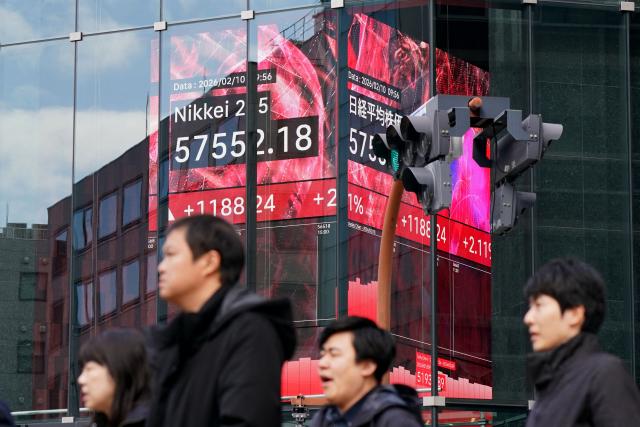 Pedestrians wait at the crosswalk traffic light below an electronic quotation board displaying numbers of the Nikkei Stock Average on the Tokyo Stock Exchange in Tokyo on February 10, 2026. (Photo by Kazuhiro NOGI / AFP)