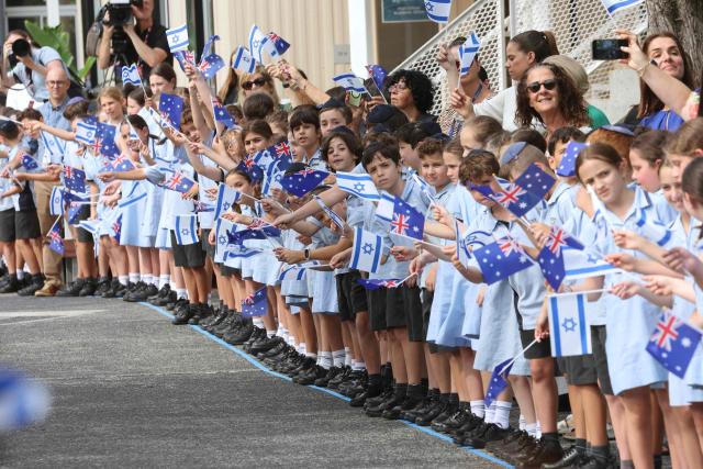 Students wave flags as they await the arrival of Israeli President Isaac Herzog at Moriah War Memorial College during his state visit to Australia in Sydney on February 10, 2026. Herzog's tightly secured, four-day trip aims to console Australia's Jewish community after the December shooting at Sydney's Bondi Beach that killed 15 people at a Hanukkah festival. (Photo by Rohan Kelly / POOL / AFP)