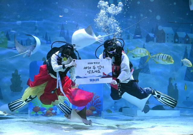 South Korean divers wearing traditional hanbok dresses hold a placard reading "Happy New Year!" during an underwater show to celebrate the upcoming Lunar New Year at the COEX aquarium in Seoul on February 10, 2026. (Photo by Jung Yeon-je / AFP)