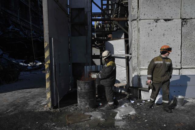 Employees warm themself near a barrel with bonfire during ongoing work to clear debris at a heavily damaged thermal power plant of the Ukrainian energy provider DTEK in an undisclosed location in Ukraine on February 9, 2026, following Russian missile and drone strikes amid the Russian invasion of Ukraine. (Photo by Genya SAVILOV / AFP)
