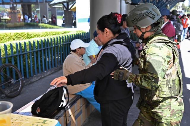 A soldier checks a woman's bag as military personnel carry out weapons and drug inspections in Quito on February 10, 2026, as part of efforts to fight crime. (Photo by Rodrigo BUENDIA / AFP)