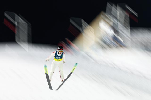 This slow shutter photograph shows China's Liu Qi jumping during the ski jumping mixed team final round of the Milano Cortina 2026 Winter Olympic Games at Predazzo Ski Jumping Stadium in Predazzo (Val di Fiemme), on February 10, 2026. (Photo by Anne-Christine POUJOULAT / AFP)