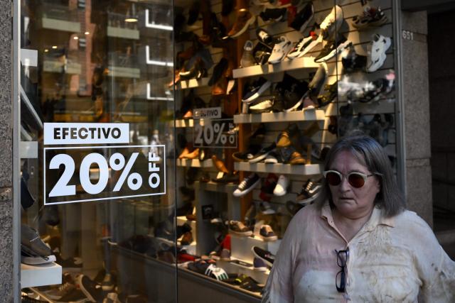 A woman leaves a shoes store past a sign on the door reading "20% off with cash" in Buenos Aires, on February 10, 2026. Inflation remained practically stable in January in Argentina, closing at 2.9%, the Indec statistics institute announced on Tuesday. Its director resigned last week after opposing the government’s decision to postpone the implementation of a new measurement method. (Photo by Luis ROBAYO / AFP)