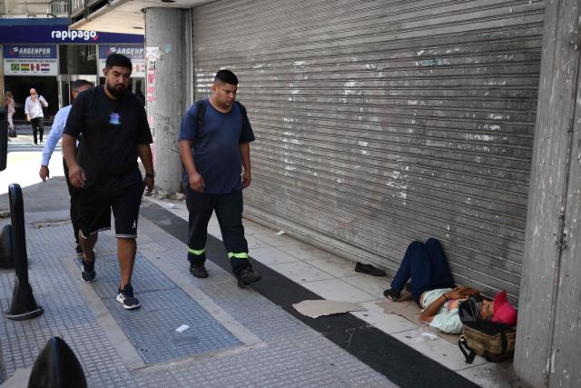 Men walk past a homeless man sleeping on a street in Buenos Aires, on February 10, 2026. Inflation remained practically stable in January in Argentina, closing at 2.9%, the Indec statistics institute announced on Tuesday. Its director resigned last week after opposing the government’s decision to postpone the implementation of a new measurement method. (Photo by Luis ROBAYO / AFP)